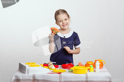 Image of Girl with smile holding a pizza cooked in kitchen