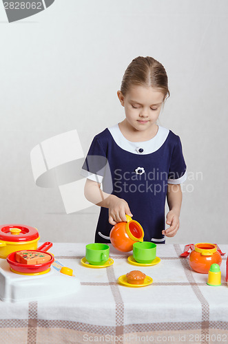 Image of Girl pouring milk into a cup of children's kitchen