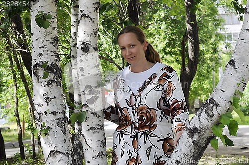 Image of The happy woman stands near birches in park.
