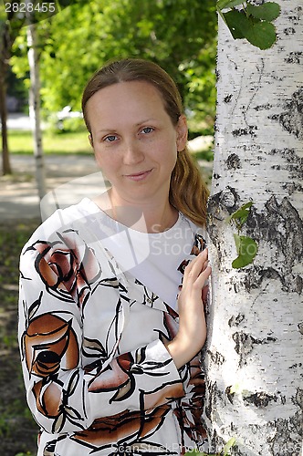 Image of The happy woman stands near birches in park.