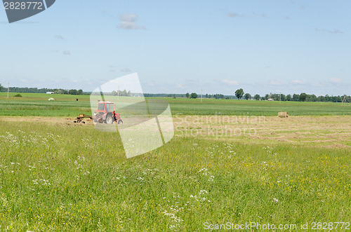 Image of Red tractor ted hay dry grass in agriculture field 