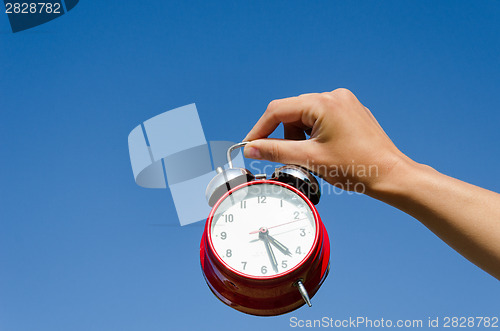 Image of hand hold chrome alarmclock on blue sky abckground 