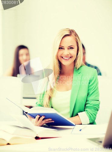 Image of smiling young woman reading book at school