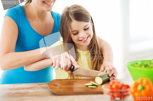 Image of smiling little girl with mother chopping cucumber