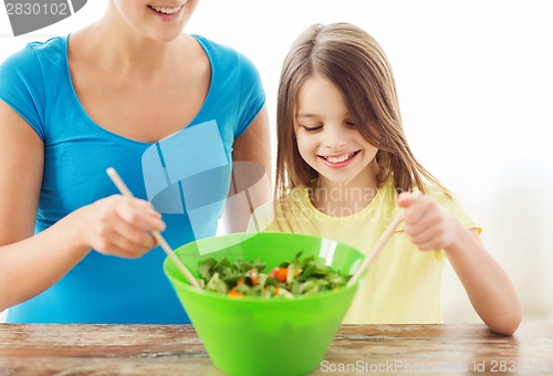 Image of little girl with mother mixing salad in kitchen