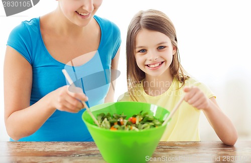 Image of little girl with mother mixing salad in kitchen