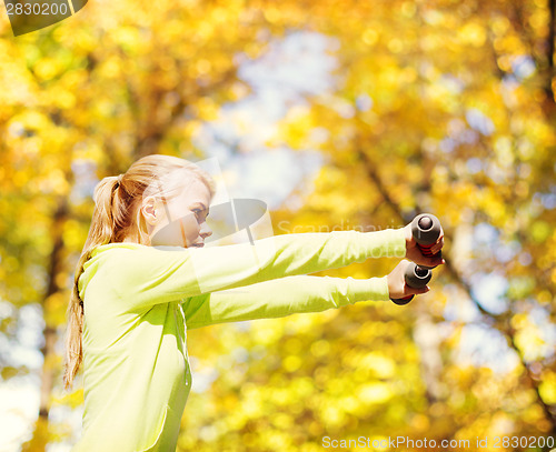 Image of sporty woman with light dumbbells outdoors