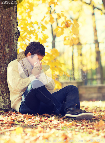 Image of ill man with paper tissue in autumn park