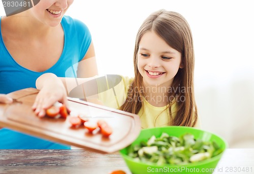 Image of little girl with mother adding tomatoes to salad