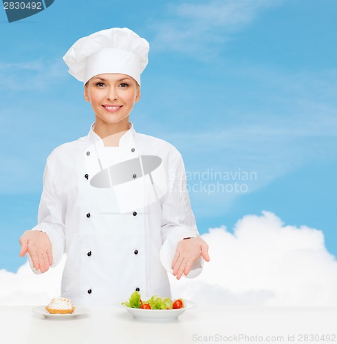 Image of smiling female chef with salad and cake on plates