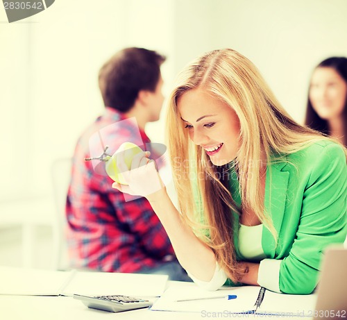 Image of smiling student girl eating apple at school