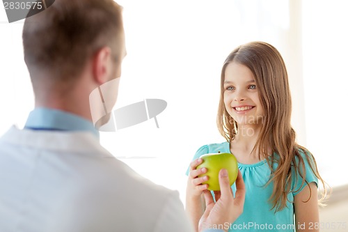 Image of male doctor giving an apple to smiling little girl