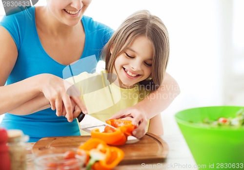 Image of smiling little girl with mother chopping pepper