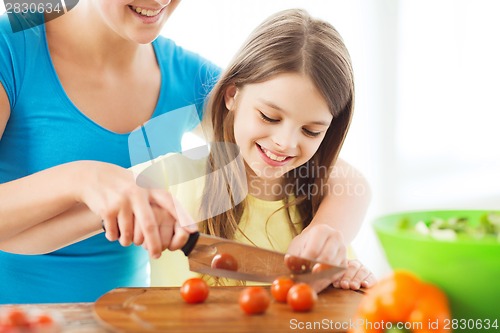 Image of smiling little girl with mother chopping tomatoes