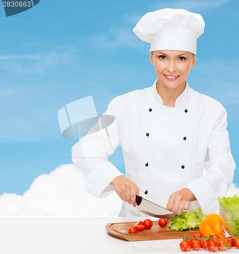 Image of smiling female chef chopping vegetables