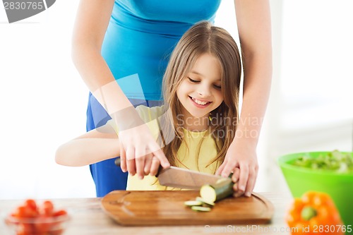 Image of smiling little girl with mother chopping cucumber