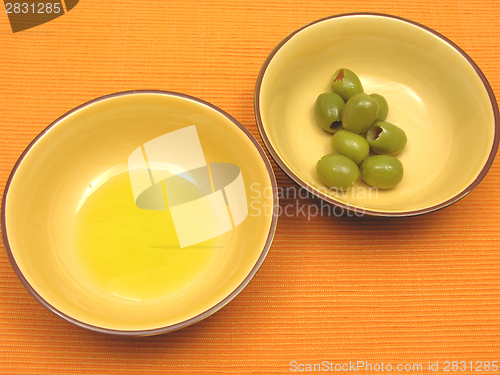 Image of Two bowls of ceramic with olive oil and olives on orange background