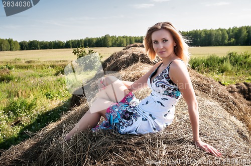 Image of Young blond woman sits on hay