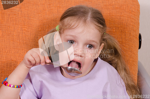 Image of Girl licks a spoon with honey