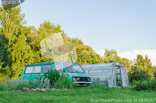 Image of mini bus parked next to village greenhouse in yard 