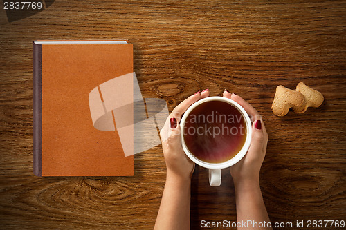 Image of woman with cup of tea, cookies and book on wood