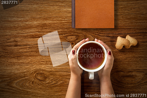 Image of woman with cup of tea, cookies and book on wood