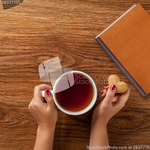 Image of woman holding hot cup of tea with cookies