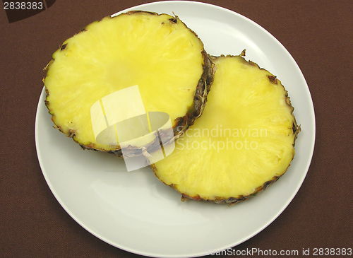 Image of Two slices of pineapple on a white plate and brown placemat