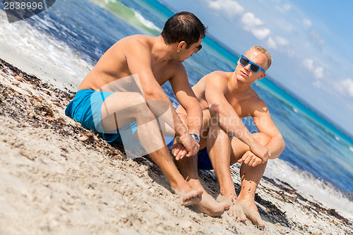 Image of Two handsome young men chatting on a beach