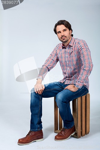 Image of Handsome young man sitting on a wooden box