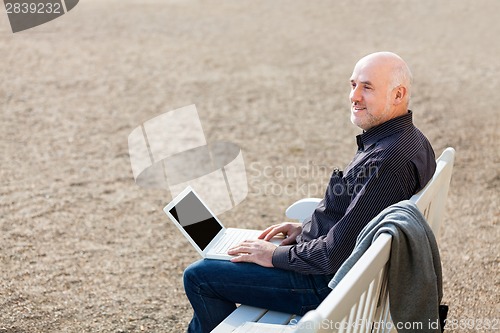 Image of Man sitting on a bench using a laptop