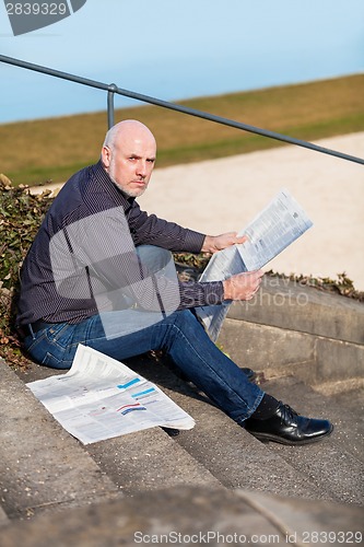 Image of Man sitting on steps reading a newspaper