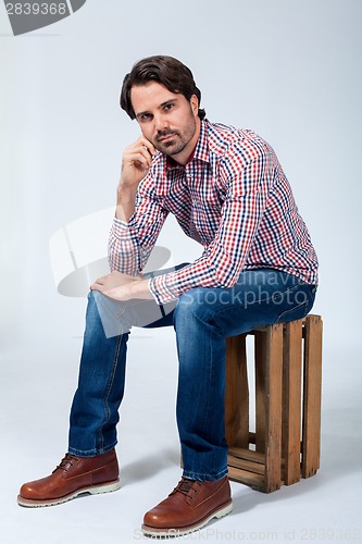 Image of Handsome young man sitting on a wooden box