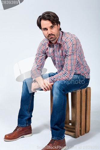 Image of Handsome young man sitting on a wooden box