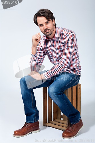 Image of Handsome young man sitting on a wooden box