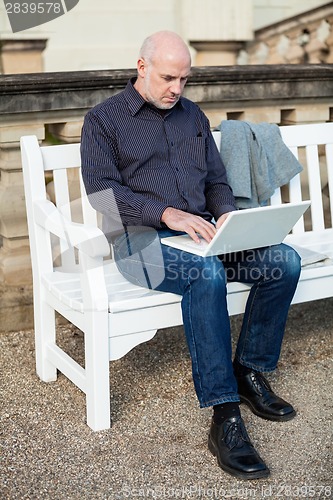 Image of Man sitting on a bench using a laptop