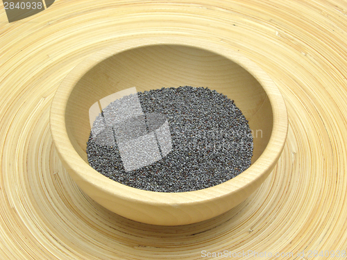 Image of Wooden bowl with poppy seeds on bamboo plate