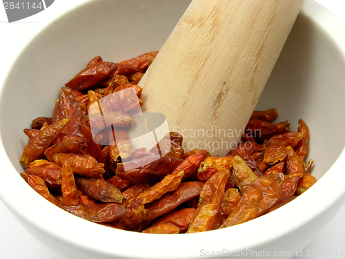 Image of Pestling dried red hot chili pepper in a bowl of chinaware