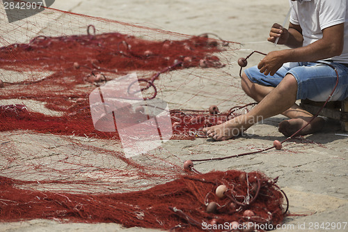 Image of Fisherman repairs his net