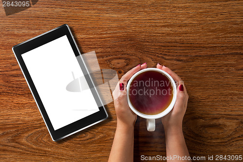 Image of woman holding cup of tea with tablet pc on wood