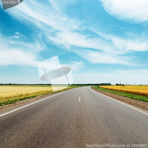 Image of asphalt road to horizon between golden fields under blue sky wit