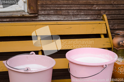 Image of two pink pail full fresh cow milk on wooden bench 