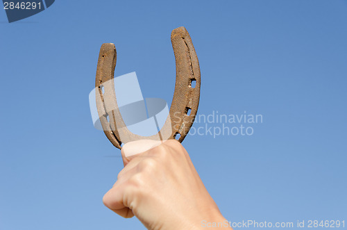 Image of hand hold horseshoe symbol of luck on blue sky 