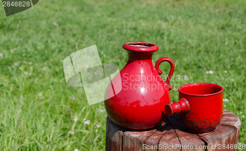Image of ceramic red water jug and cup on stump on nature  