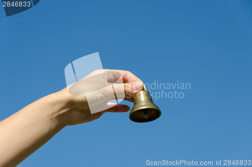 Image of hand hold brass old jingle  on blue sky background 