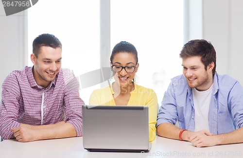 Image of three smiling colleagues with laptop in office