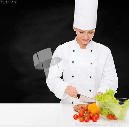 Image of smiling female chef chopping vegetables