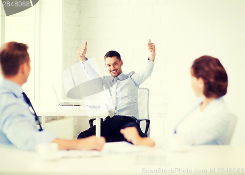 Image of happy businessman showing thumbs up in office