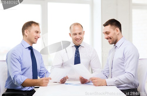 Image of smiling businessmen with papers in office
