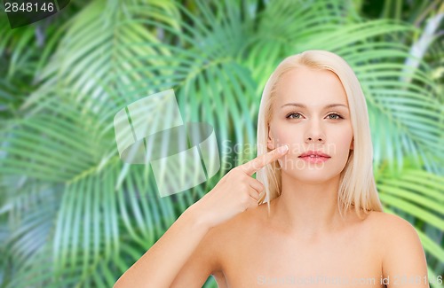 Image of calm young woman pointing at her cheek